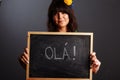 Latin brazil lady in a soccer clothes holding a small blackboard with Hello word on his native language isolated on gray