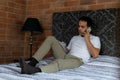 Latin Colombian man sitting on his bed writing in a notebook and making a phone call Royalty Free Stock Photo