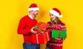 Latin father and daughter in red sweater Christmas santa hat holding christmas presents and gifs on yellow background in Mexico La