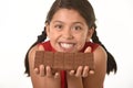 Latin female child holding with both hands big chocolate bar in front of her happy smiling face Royalty Free Stock Photo