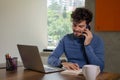 latin freelancer in casual office making phone call while working with laptop and taking notes Royalty Free Stock Photo