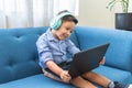 Latin little boy with headphones in a laptop video conference sitting on a blue sofa Royalty Free Stock Photo