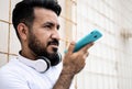 Latin man with a beard, recording a voice message on his cell phone leaning against a wall. Royalty Free Stock Photo