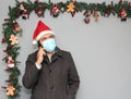 Latin man with protection mask, coat and Santa Claus hat in video call with cell phone and Christmas decoration, new normal covid Royalty Free Stock Photo