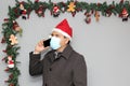 Latin man with protection mask, coat and Santa Claus hat in video call with cell phone and Christmas decoration, new normal covid Royalty Free Stock Photo