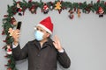 Latin man with protection mask, coat and Santa Claus hat in video call with cell phone and Christmas decoration, new normal covid Royalty Free Stock Photo