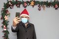 Latin man with protection mask, coat and Santa Claus hat in video call with cell phone and Christmas decoration, new normal covid Royalty Free Stock Photo