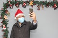 Latin man with protection mask, coat and Santa Claus hat in video call with cell phone and Christmas decoration, new normal covid Royalty Free Stock Photo