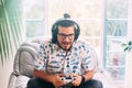 Latin man sitting on the sofa, surprised while playing on his console. He has headphones and controller Royalty Free Stock Photo