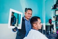 Latin man stylist cutting hair to a client and holding a mirror in a barber shop in Mexico Royalty Free Stock Photo