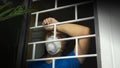 Latin man with white face mask inside his house looking out through the window, leaning against security bars