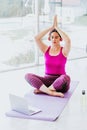 Latin mature woman with headphones doing yoga with closed eyes listening to a guided meditation on laptop in Mexico