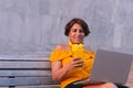 Latin Mature woman using a cell phone and laptop while sitting on a bench in the park