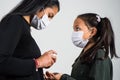 Latin mother applies disinfectant to her daughter to prevent infection, the two girls wear a protective mask. Infection