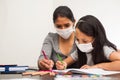 Latin mother helps her daughter with the homework on a black table at home, wears prevention mask. Teleworking and studying at