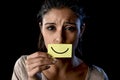 Latin sad depressed latin girl holding paper hiding her mouth behind fake drawn smile Royalty Free Stock Photo