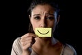 Latin sad depressed latin girl holding paper hiding her mouth behind fake drawn smile Royalty Free Stock Photo