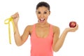 Latin sport woman in fitness clothes holding apple fruit and measure tape smiling happy