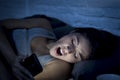 Latin woman on bed late at night texting using mobile phone yawning sleepy and tired Royalty Free Stock Photo