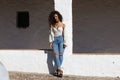 Latin woman with dark, curly hair and middle-aged dressed in jeans and white lace top is leaning on a column of a Mediterranean Royalty Free Stock Photo