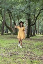 Latin woman with dress and hat walking through a park with trees