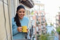 Latin woman drinking cup of coffee or tea smiling happy at apartment window balcony Royalty Free Stock Photo