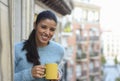 Latin woman drinking cup of coffee or tea smiling happy at apartment window balcony Royalty Free Stock Photo