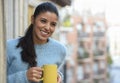 Latin woman drinking cup of coffee or tea smiling happy at apartment window balcony