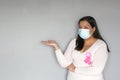 Latin woman with protection mask, black hair and white sweater with pink ribbon for campaign against breast cancer Royalty Free Stock Photo