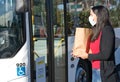 Latin woman wearing face mask and holding a shopping bag at the bus stop during pandemic covid-19