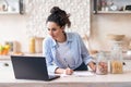 Latin woman writing new recipe watching online lessons on laptop in light kitchen interior, copy space Royalty Free Stock Photo