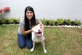 Latin young adult woman with long straight black hair is very happy accompanied by her friend a white pitbull dog with brown spots
