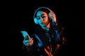 Latin young woman with headphones listening to music over color neon and black background in Mexico Latin America