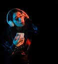 Latin young woman with headphones listening to music over color neon and black background in Mexico Latin America