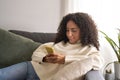 Latin young woman sitting on couch using mobile phone at home. Royalty Free Stock Photo