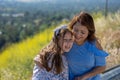 Latina Mother and Daughter Smiling and laughing on a hill in front of yellow flowers