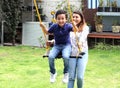 Latina woman mom and 6 year old boy with covid-19 virus protection mouthpieces, playing swing in the garden Royalty Free Stock Photo