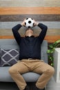 Latino adult man with glasses watches soccer game on TV on his sofa with his ball and gets angry and sad watching the football gam