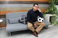 Latino adult man with glasses watches soccer game on TV on his sofa with his ball and gets angry and sad watching the football gam