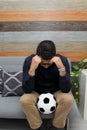 Latino adult man with glasses watches soccer game on TV on his sofa with his ball and gets excited, angry, sad watching the soccer