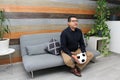 Latino adult man with glasses watches soccer game on TV on his sofa with his ball and gets excited, angry, sad watching the soccer