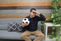 Latino adult man with glasses watches soccer game on TV on his sofa with his ball and gets excited, angry, sad watching the soccer