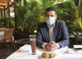 Latino adult man with protection mask in restaurant with drink and food, new normal covid-19