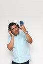 Latino adult man uses technology with his cell phone and headphones to listen to music, play video games, make video calls, watch Royalty Free Stock Photo