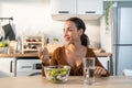 Latino attractive woman wear apron eat green salad in kitchen at home. Young beautiful girl feeling happy and enjoy eating Royalty Free Stock Photo