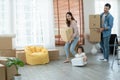 Latino father with beard, Asian mother and little cute daughter carrying packed cardboard boxes into their new home with happiness