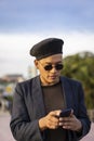 Latino gay male with makeup on wearing trendy hat looking at cell phone