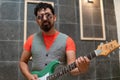 Latino musician with rocker style posing with his green guitar dressed in an orange shirt and vest on a gray background with Royalty Free Stock Photo