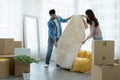 Latino man and Asian woman couple unpack and spread white fluffy carpet while move to new house together. Mixed race family