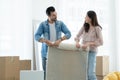 Latino man with beard and Asian woman couple packing and rolling white fluffy carpet while move to new house. Mixed race family